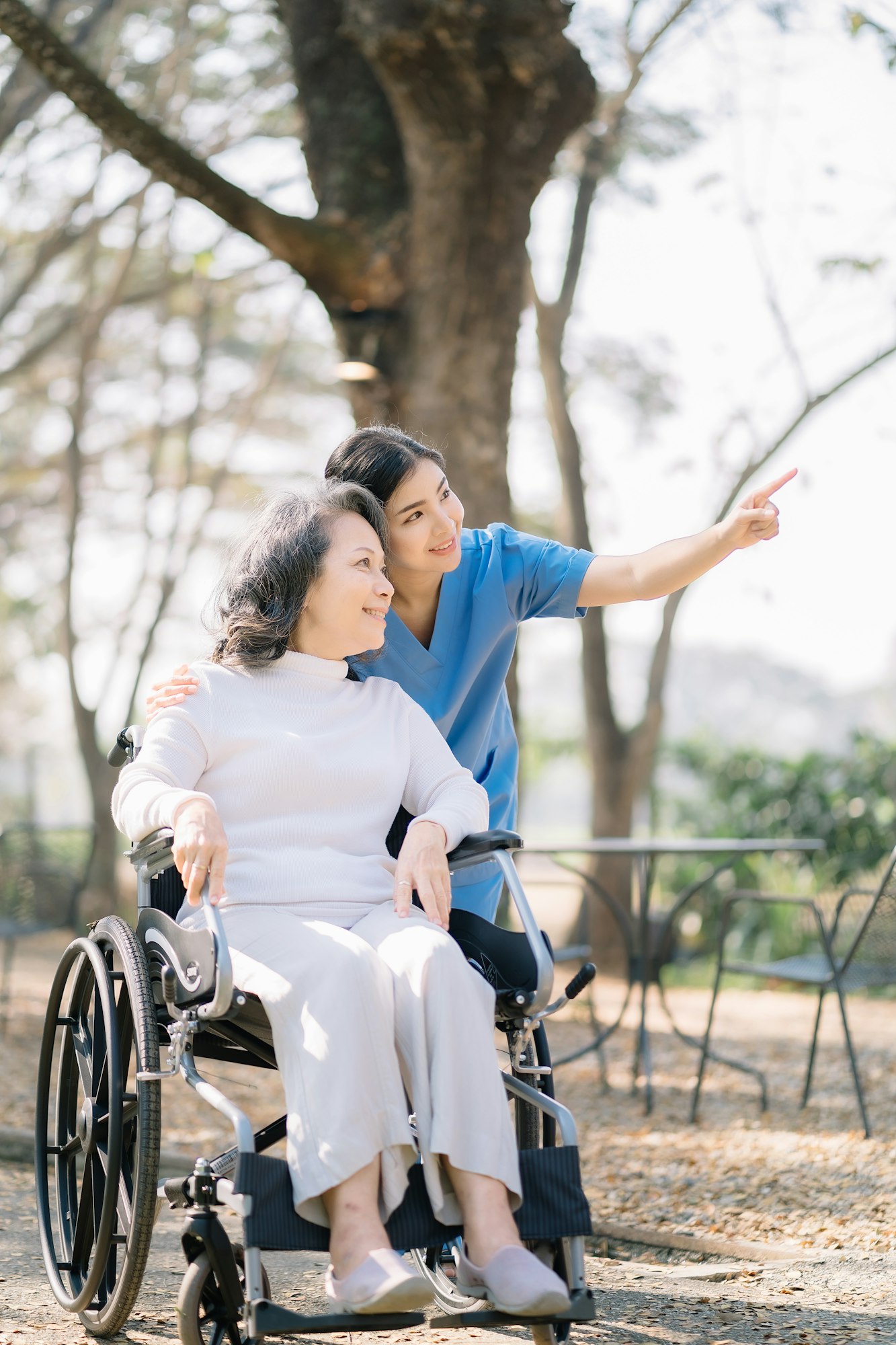 Smiling physiotherapist taking care of the happy senior patient in wheelchair, outdoor.